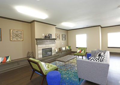The Villages at Fiskville community center with fireplace, grey couch, and green accent chairs
